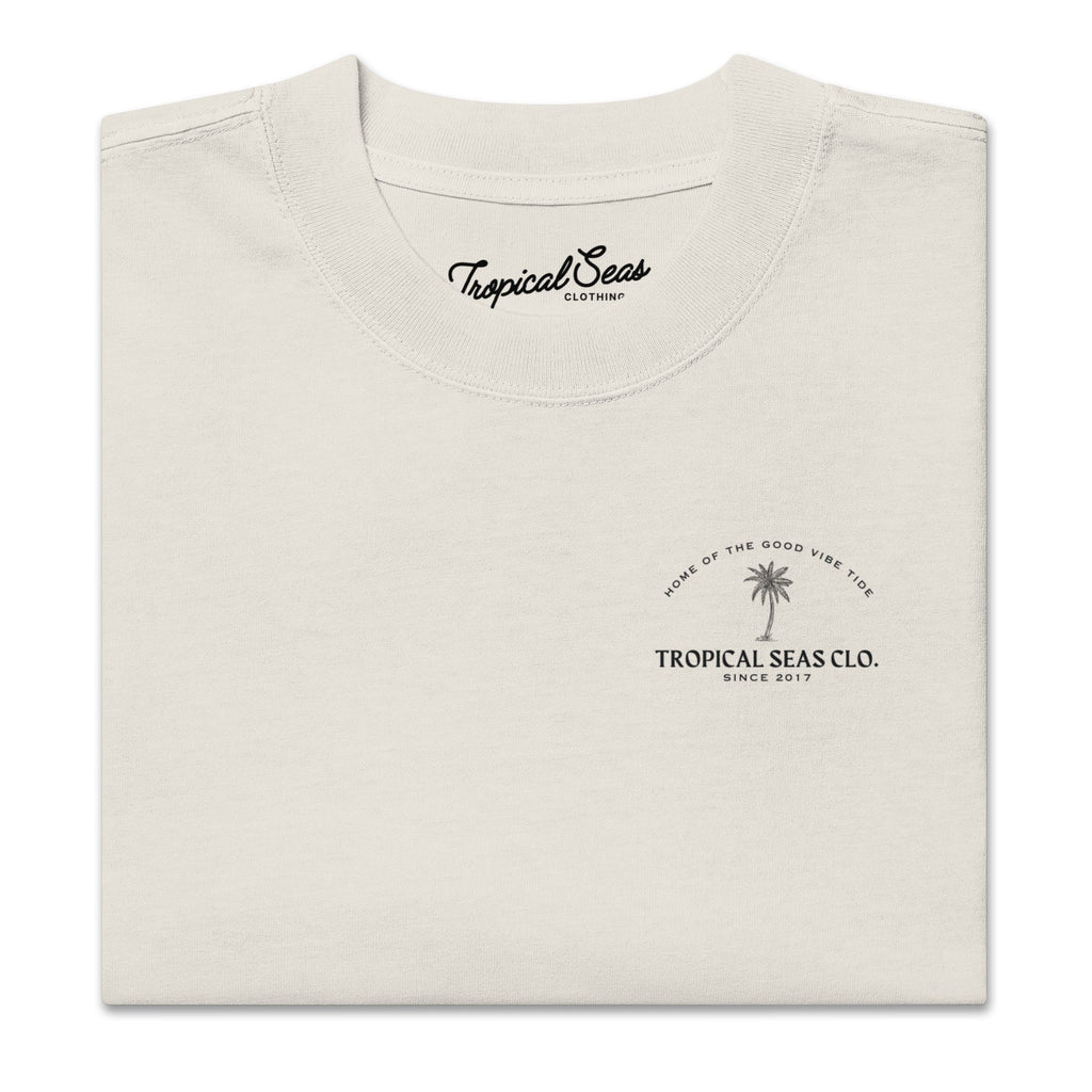 Faded cream oversized t-shirt with a palm tree graphic and "Tropical Seas Clo." text, featuring a wide neck and dropped shoulders.