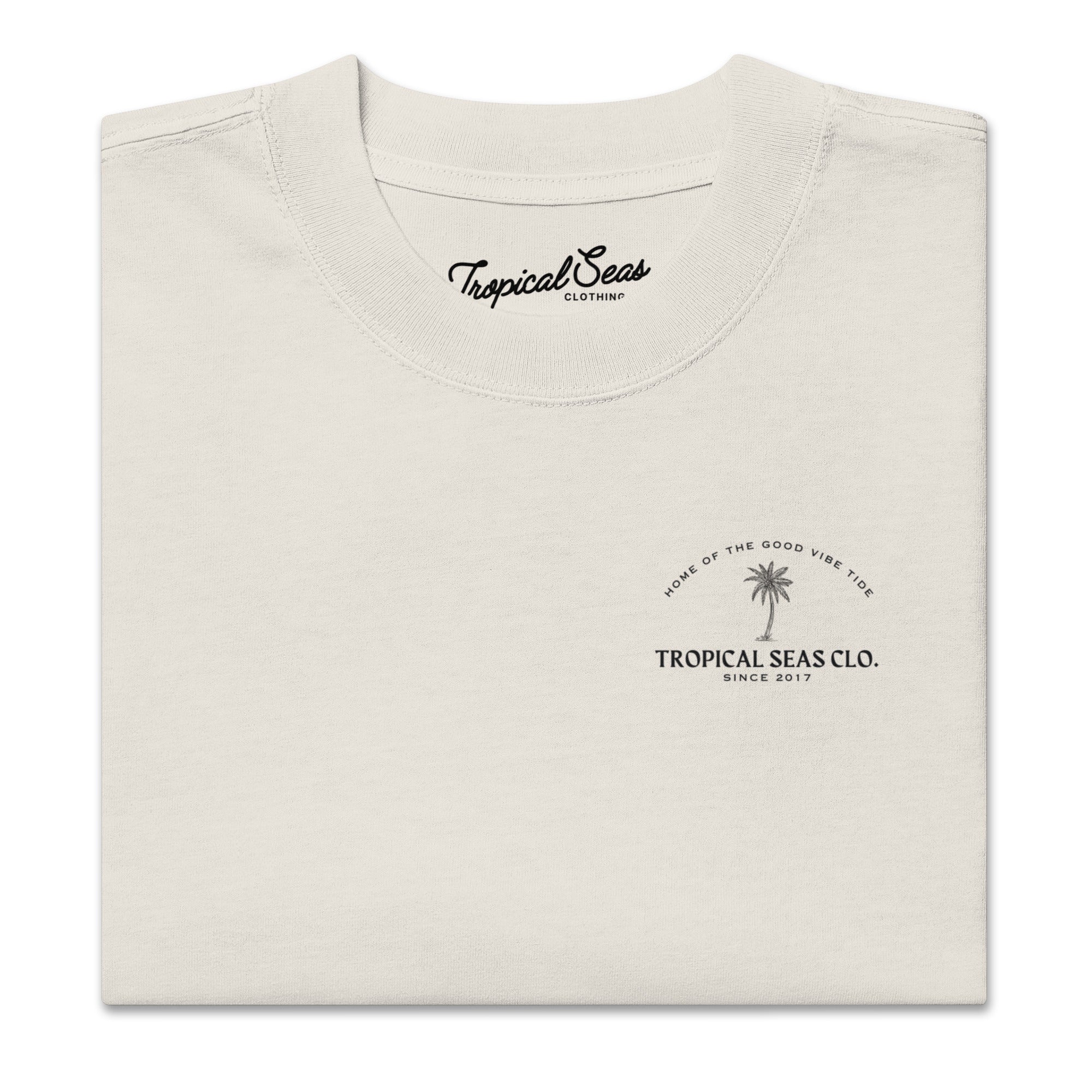 Faded cream oversized t-shirt with a palm tree graphic and "Tropical Seas Clo." text, featuring a wide neck and dropped shoulders.
