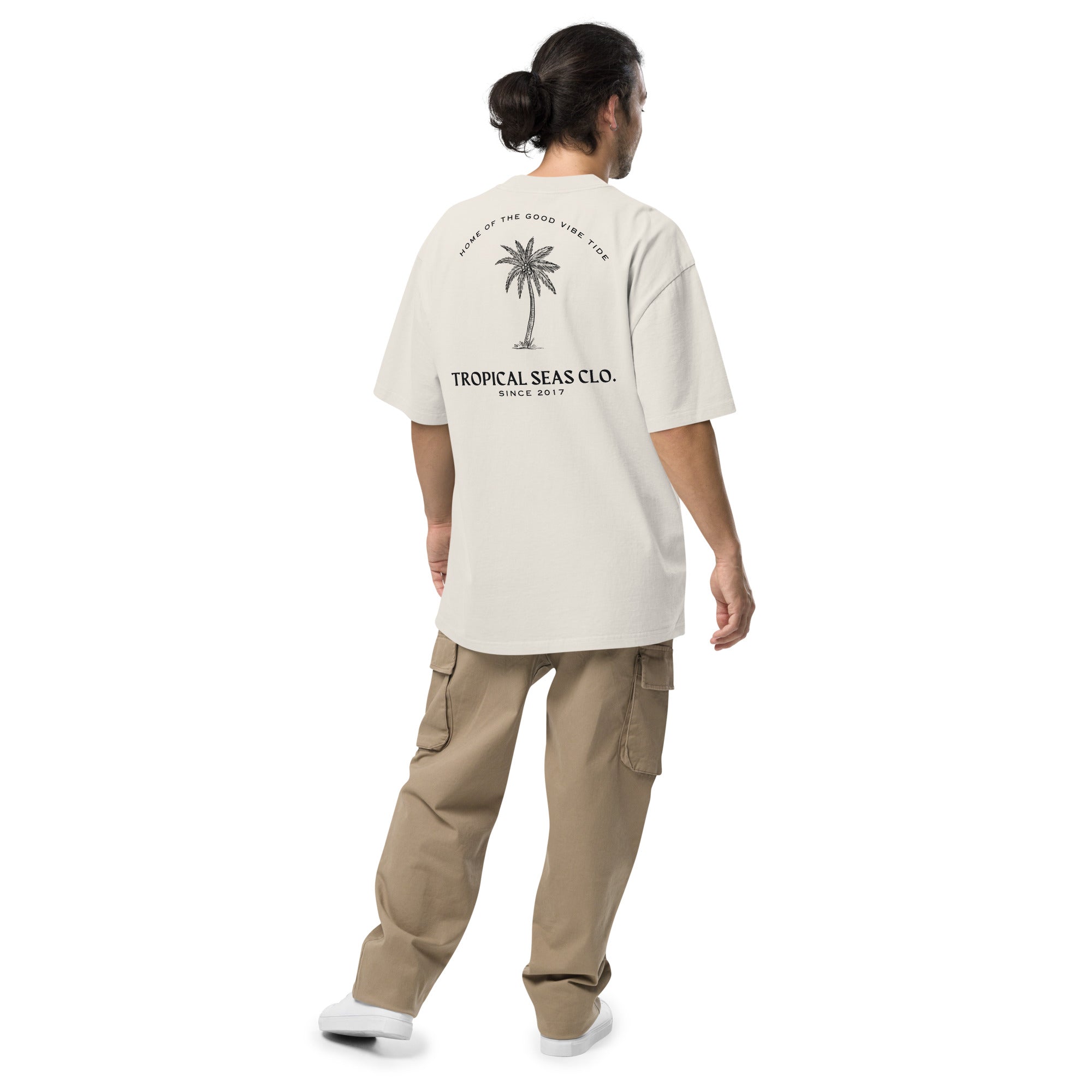 Oversized faded t-shirt in cream with a palm tree graphic and "TROPICAL SEAS CLO." text on the back, worn with cargo pants.