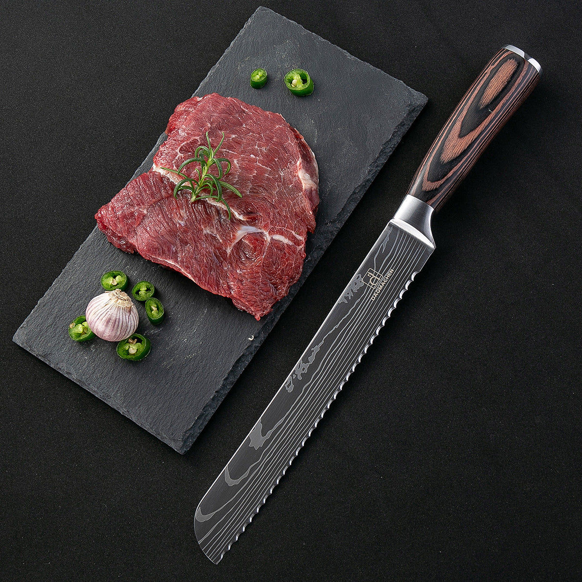 Damascus style kitchen knife beside a slab of raw beef, garnished with garlic, green chilies, and rosemary on a slate board.