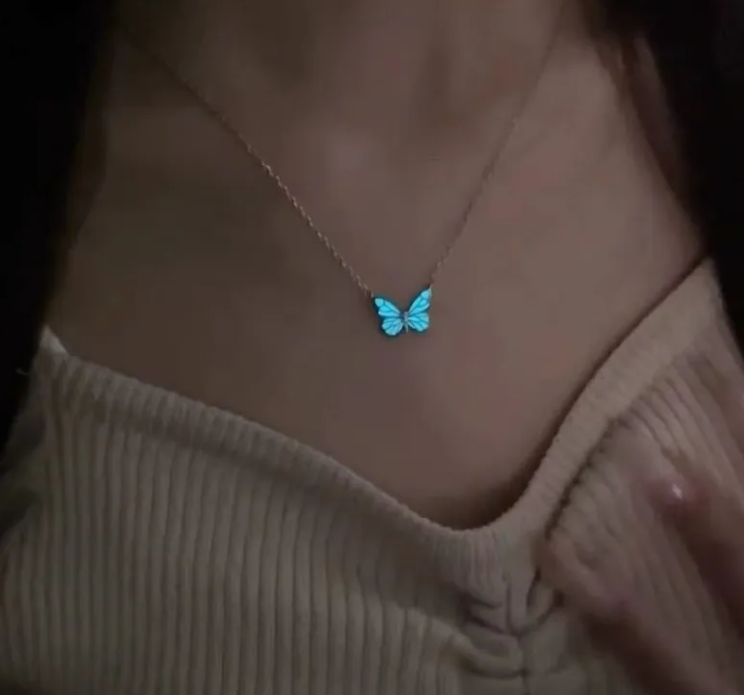 Fluorescent blue butterfly necklace on a model, worn with a soft beige top, showcasing its cross chain design.