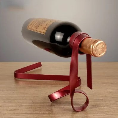 Creative floating wine rack designed like a ribbon, holding a bottle of wine in a rich burgundy color on a wooden surface.