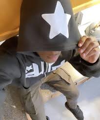 Star printed zip-up hoodie in dark color, featuring a large white star on the hood, relaxed fit, worn casually with olive pants.