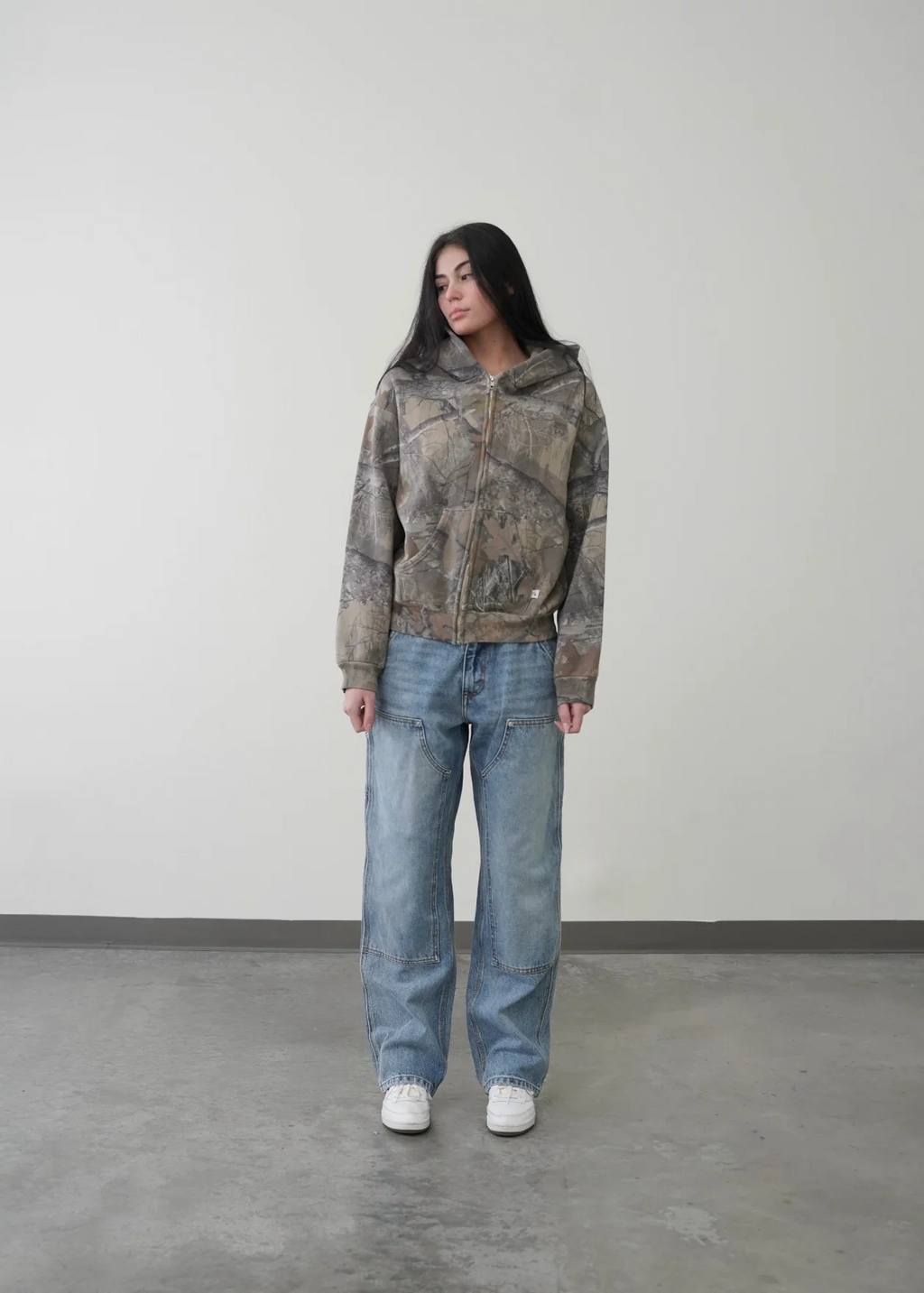 Unisex oversized hoodie in a camouflage print, featuring a zip-up front and an adjustable hood, paired with loose denim jeans.