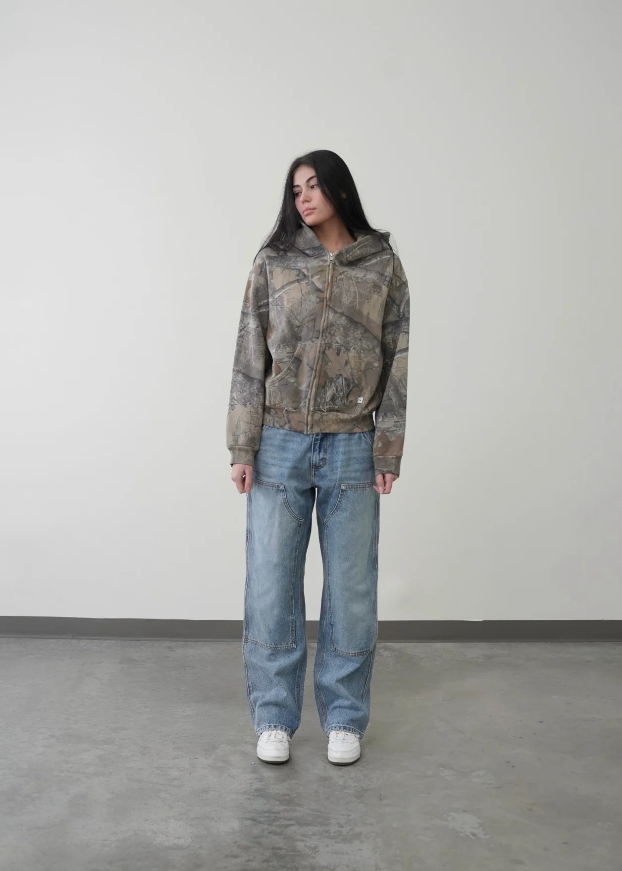 Unisex oversized hoodie in a camouflage print, featuring a zip-up front and an adjustable hood, paired with loose denim jeans.