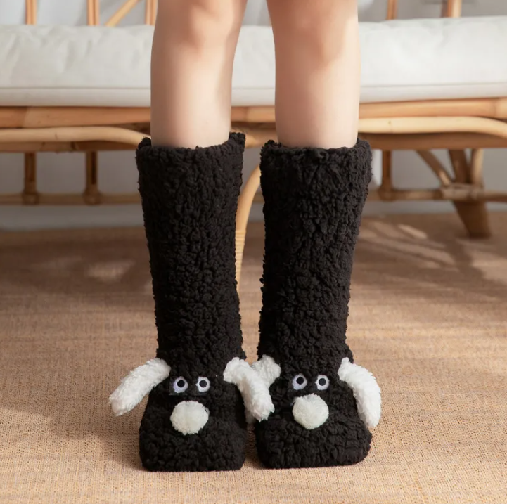 Black plush dog socks feature a cozy texture with white ears and eyes, extending calf-high for warmth and comfort.