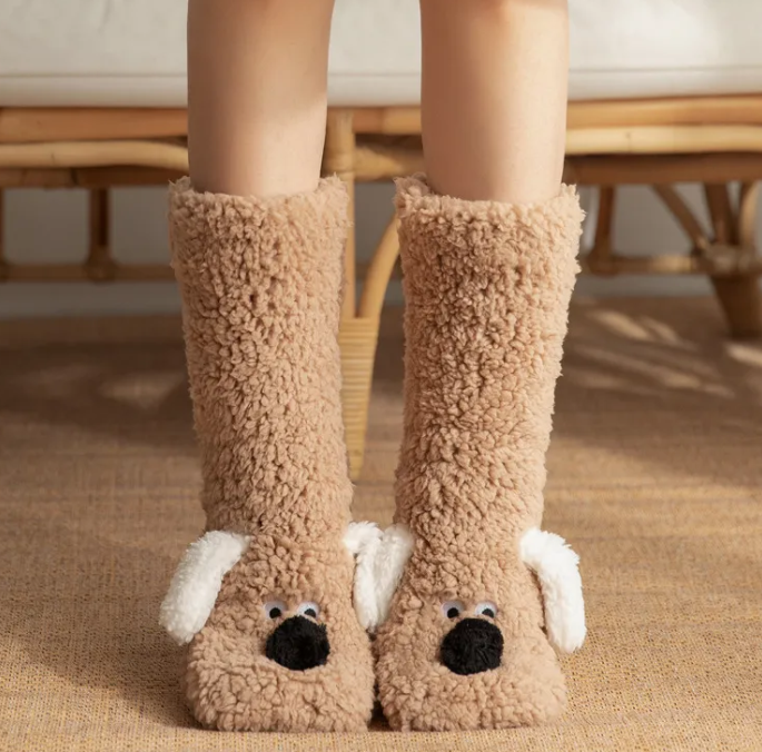 Soft plush dog socks in light brown with white ears and black nose, providing warmth and comfort for indoor use.