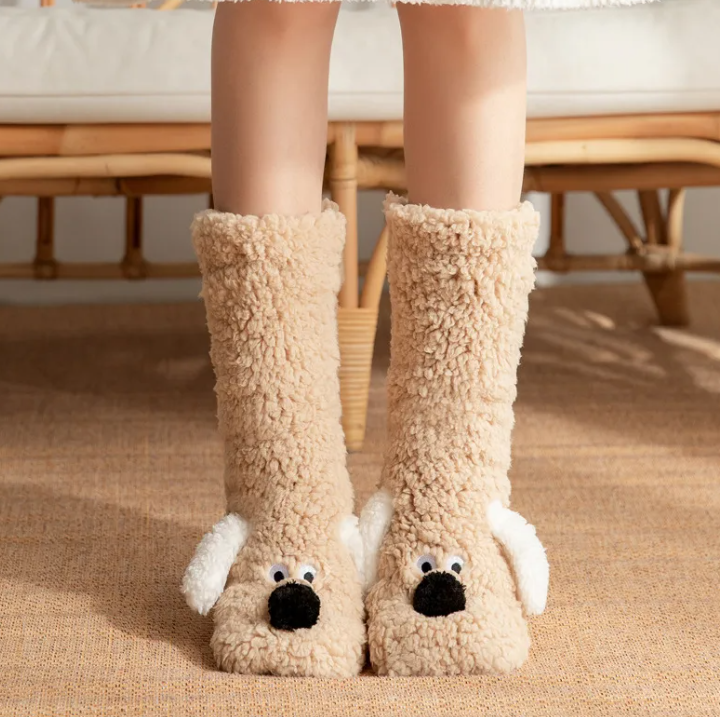 Plush beige dog socks with furry texture and playful dog face details, featuring white ears and a non-slip sole.