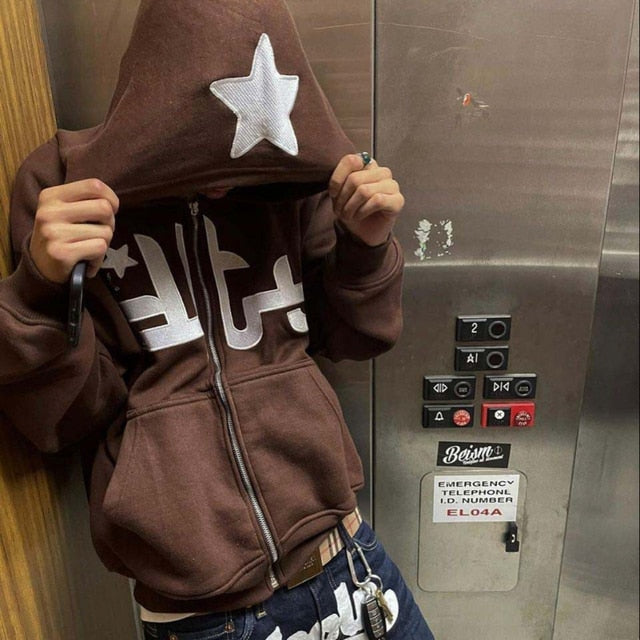 Brown zip-up hoodie featuring a large white star on the hood, worn casually with hands partially hidden inside.