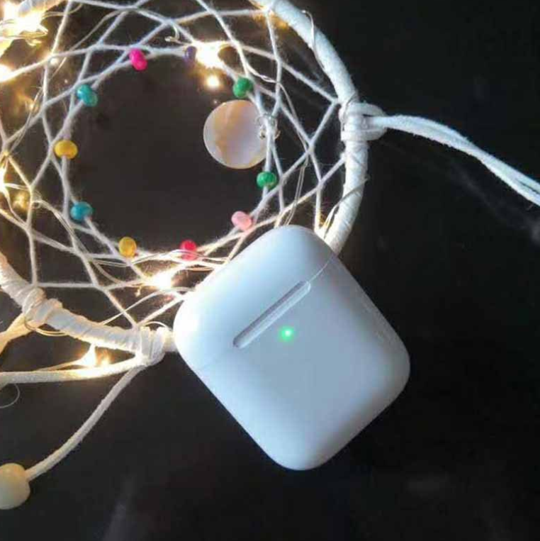 White charging case for i80 TWS Bluetooth earbuds displayed on a dark surface, surrounded by colorful lights and a dreamcatcher.