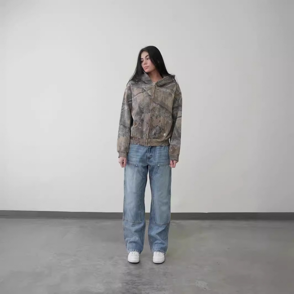 Oversized hoodie in a camouflage print, paired with relaxed blue jeans and white sneakers, showcasing a casual streetwear look.