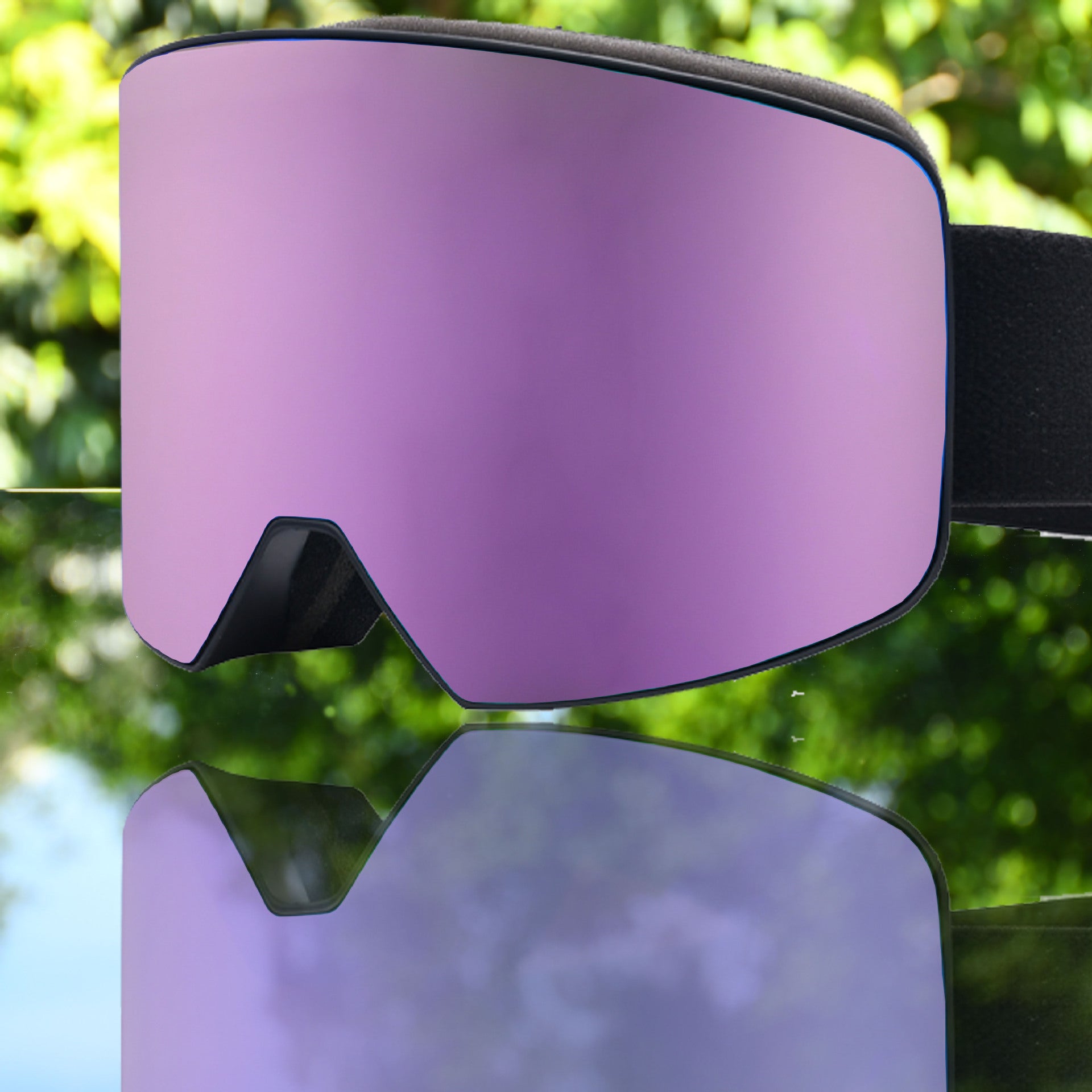Ski goggles with a large purple lens, black frame, and adjustable strap, reflecting outdoor greens.